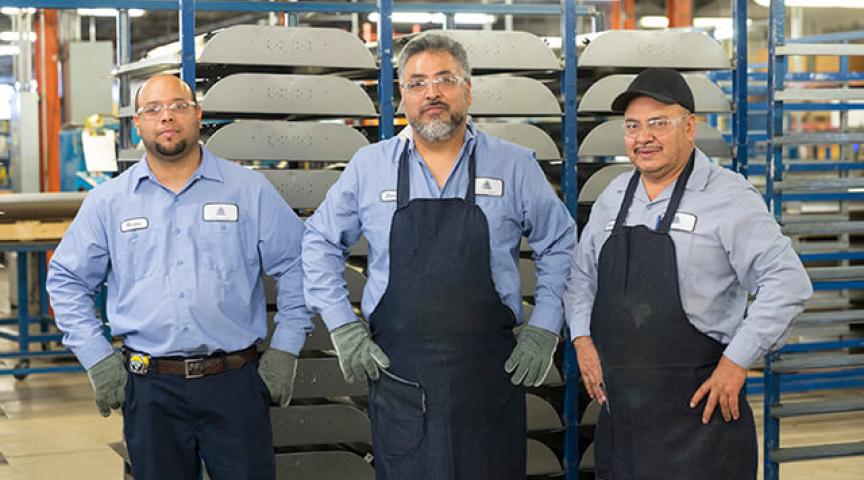 Group of 3 machinists pose with hands at hips in front of rack of housings