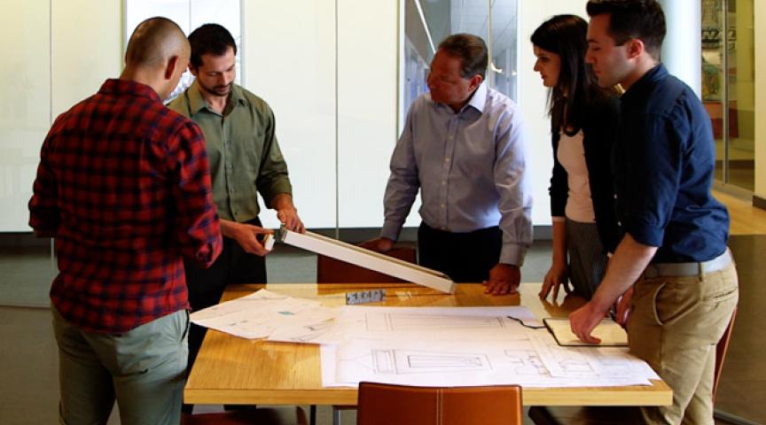 Group of Engineers and Industrial Designers meet over a table with drawings and prototypes