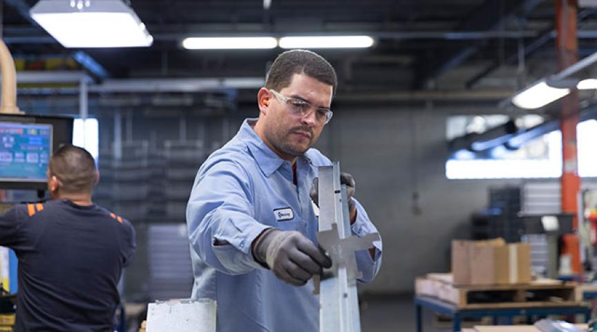 Quality: Plant worker eyes a jig for accuracy on a linear metal part